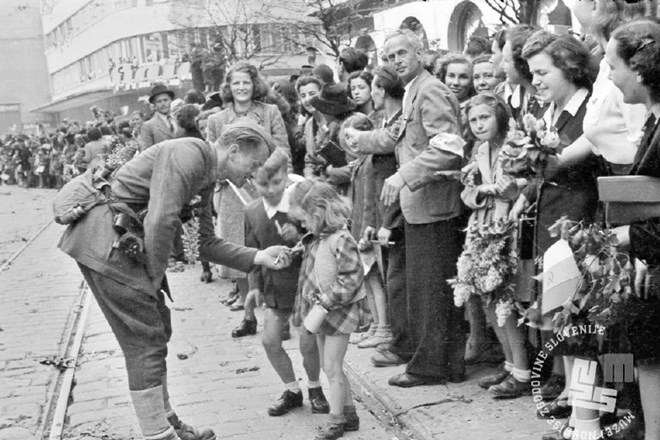 Množica pozdravlja partizane, otroci dajejo partizanu cigarete. 9. maj 1945. (Foto: Maksimiljan Zupančič, hrani: Muzej...